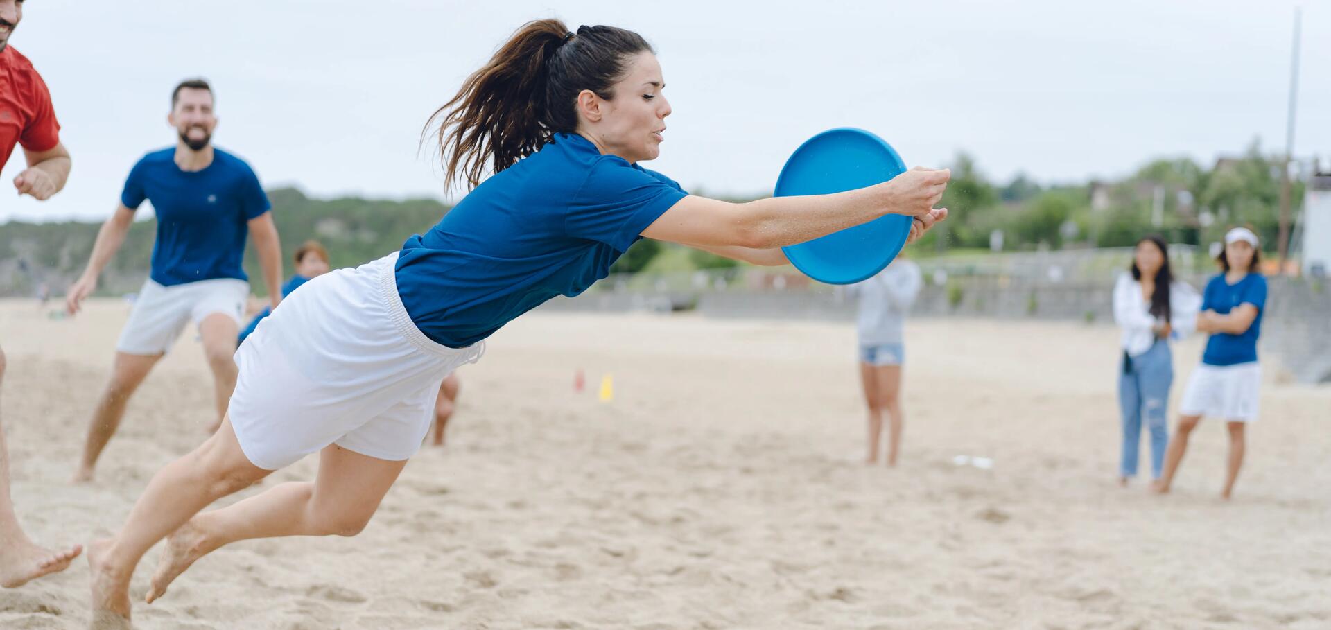 kobieta w stroju sportowym łapiąca frisbee na plaży 