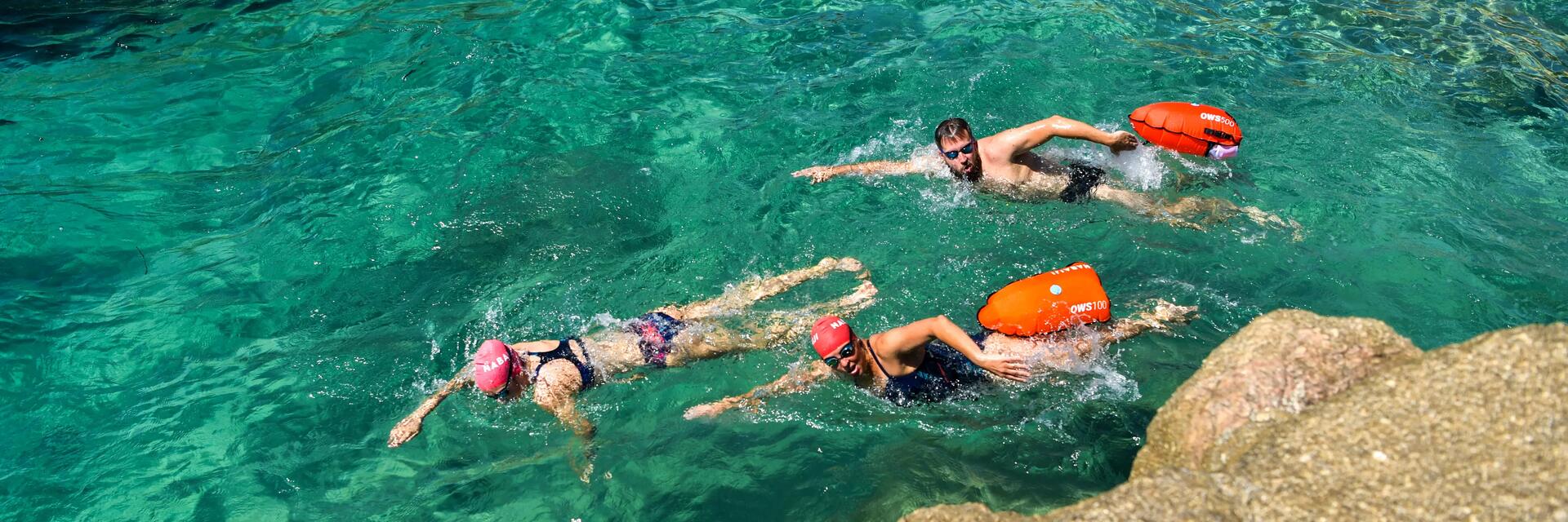 Sportowcy pływający w morzu z bojką asekuracyjną z suchą komorą