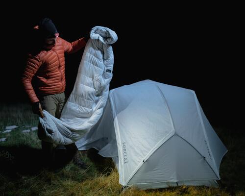 mężczyzna  z latarką czołową rozkładający śpiwór przed namiiotem