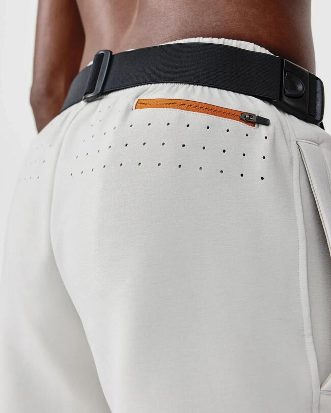 Beige Shorts mit schwarzem Gürtel, orangefarbener Reißverschluss und kleinen Belüftungslöchern.