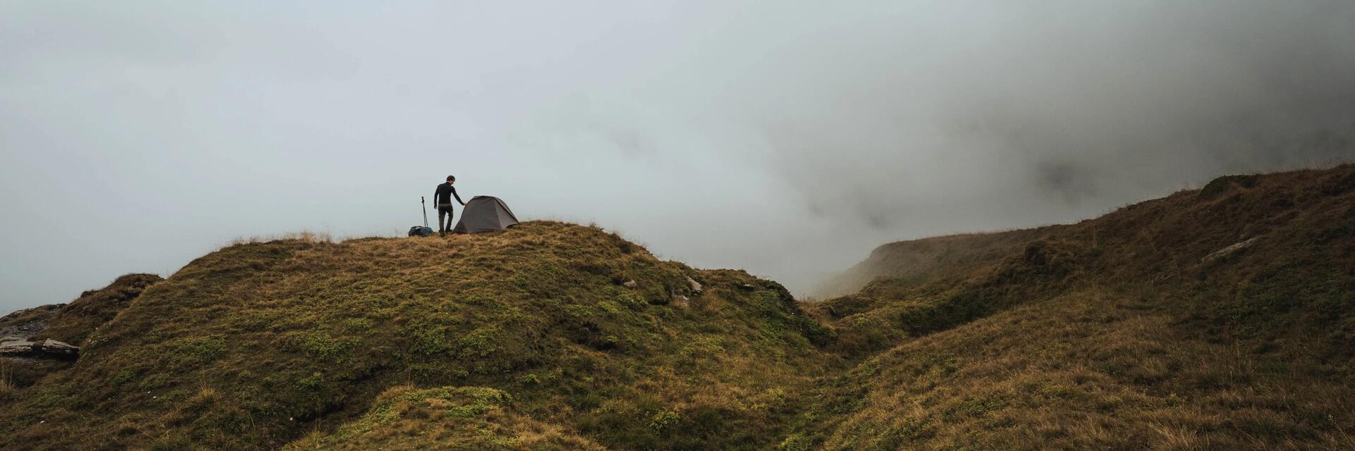 Mężczyzna stojący obok rozłożonego w plenerze namiotu podczas burzy