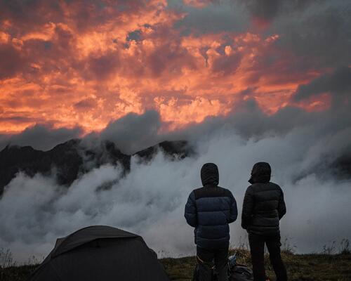 osoby w kurtkach trekkingowych stojące obok namiotu w górach