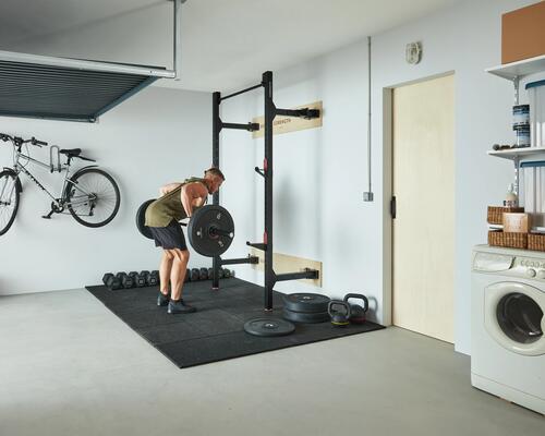 Mężczyzna w stroju sportowym ćwiczący wiosłowanie sztangą w domowej siłowni