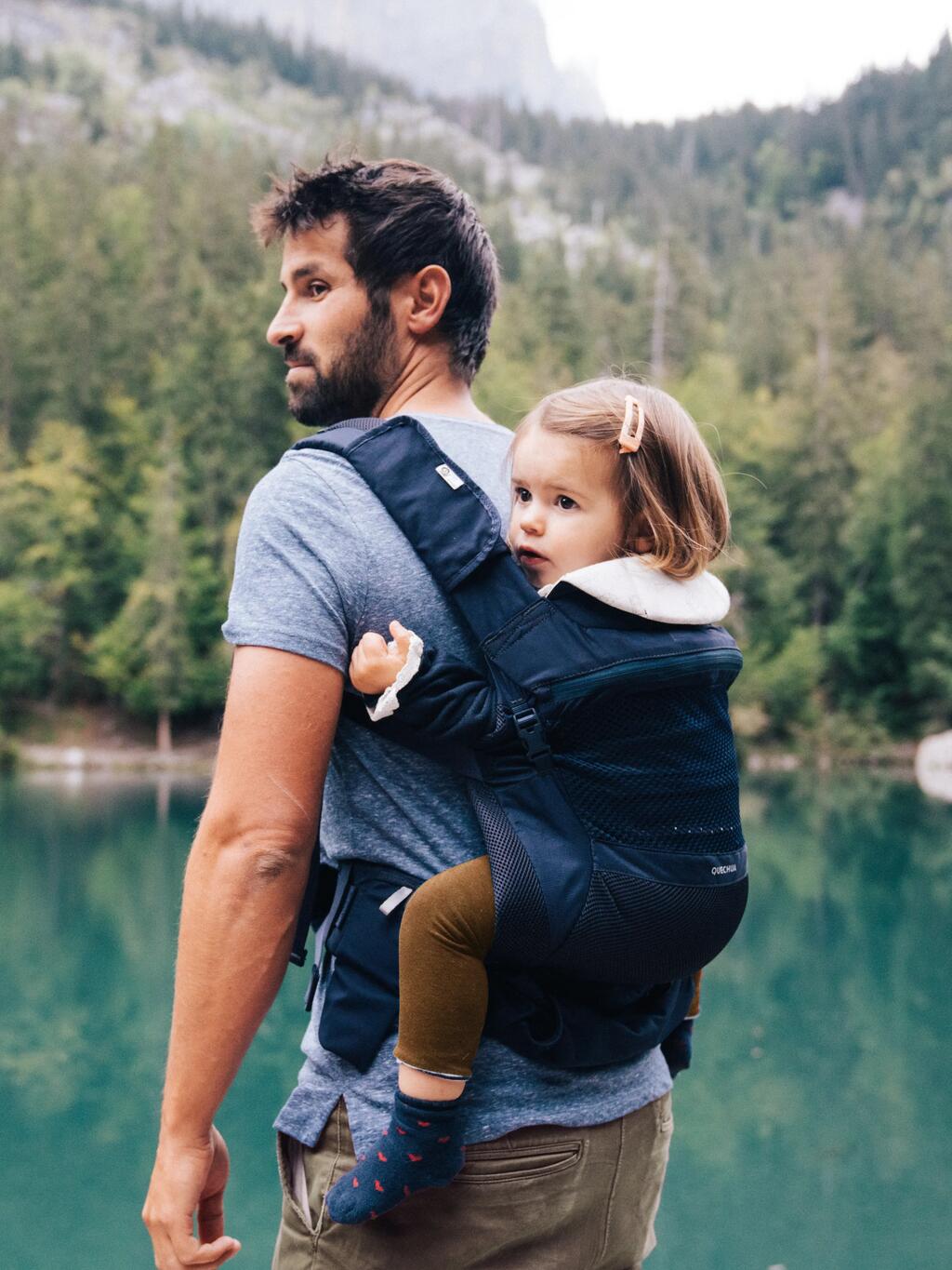 Oče v nosilki na hrbtu nosi hčerko na sprehodu ob jezeru.