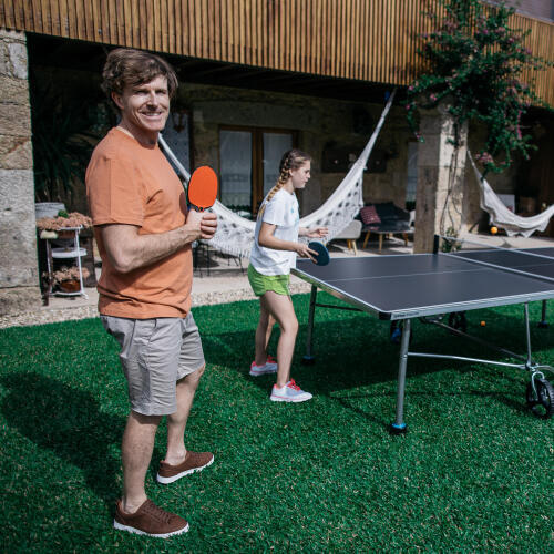 Spieler mit einem PONGORI Schläger neben der Outdoor-Tischtennisplatte PPT 530.2 OUTDOOR BLAU