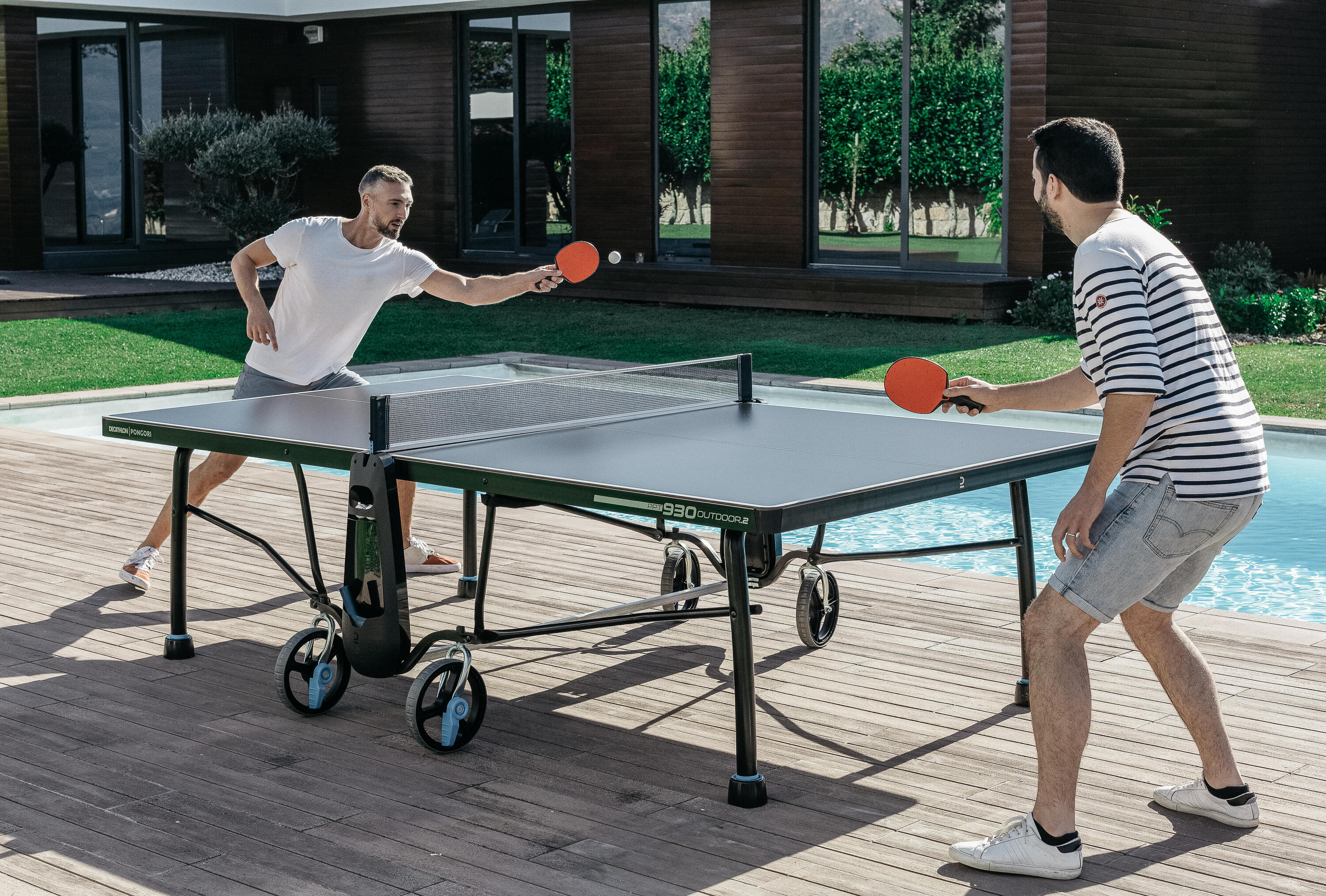 Zwei Männer spielen in einem Garten Tischtennis.