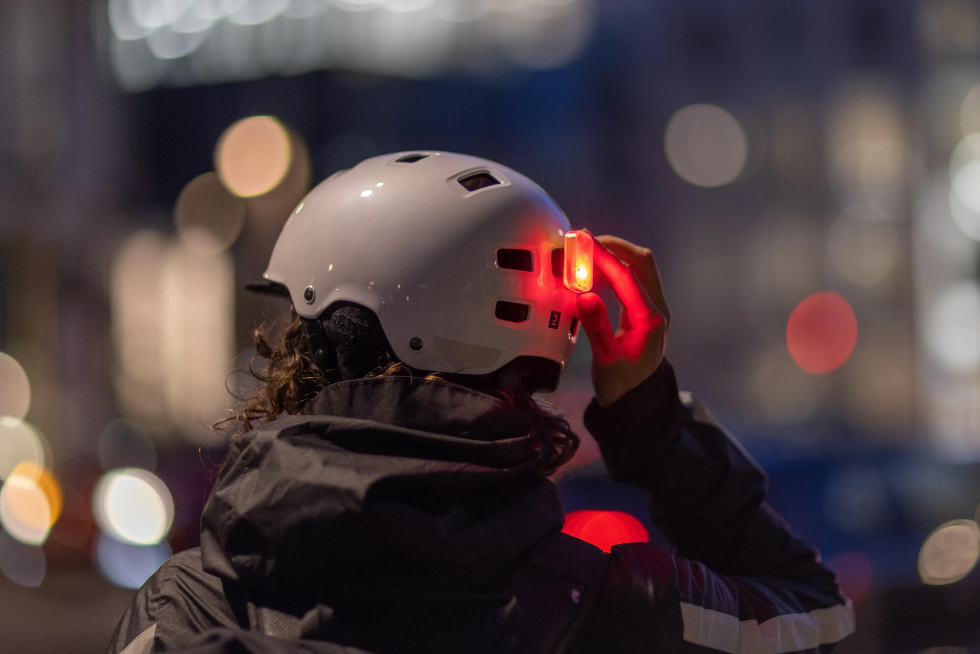 Osoba włączająca czerowną lampkę rowerową zamontowaną na kasku rowerowym