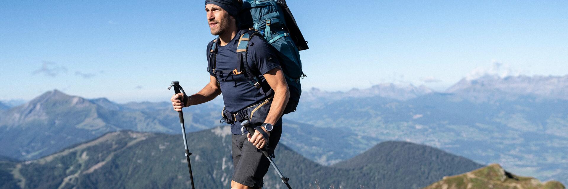 Mężczyzna z kijkami trekkingowymi i z plecakiem wędrujący po górach