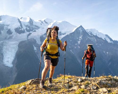 mężczyzna i kobieta w butach trekkingowych z kijkami w rękach chodzą po górach