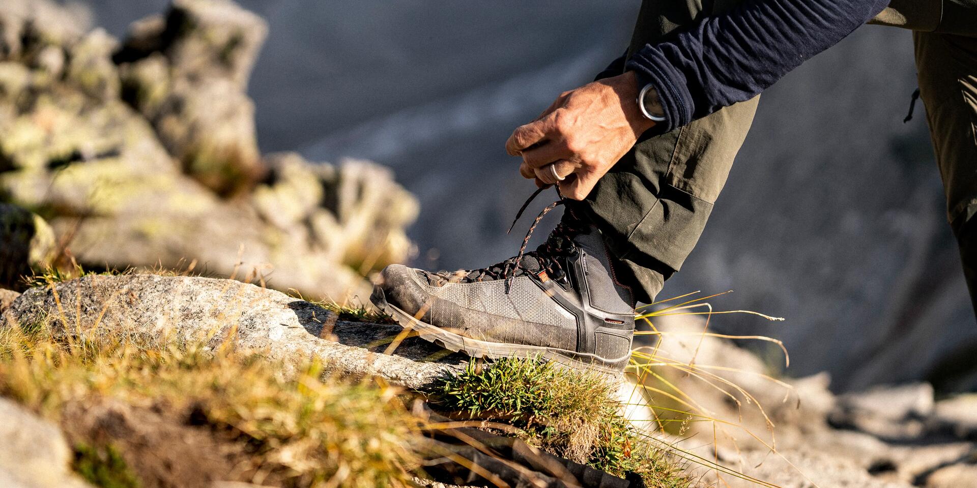 mężczyzna zawiązujący buty trekkingowe stawiając stopę kamieniu