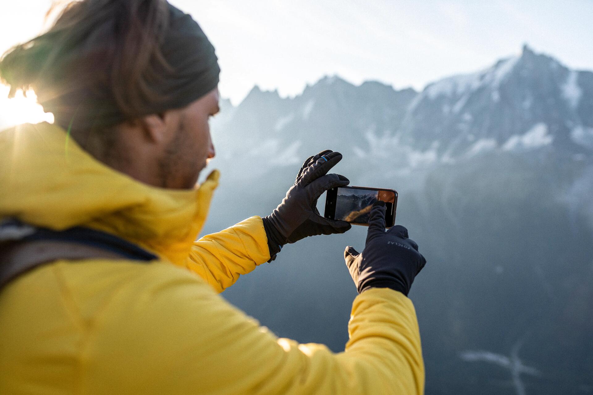 Mężczyzna w rękawiczkach robiący zdjęcie górskim widokom podczas pieszej wędrówki