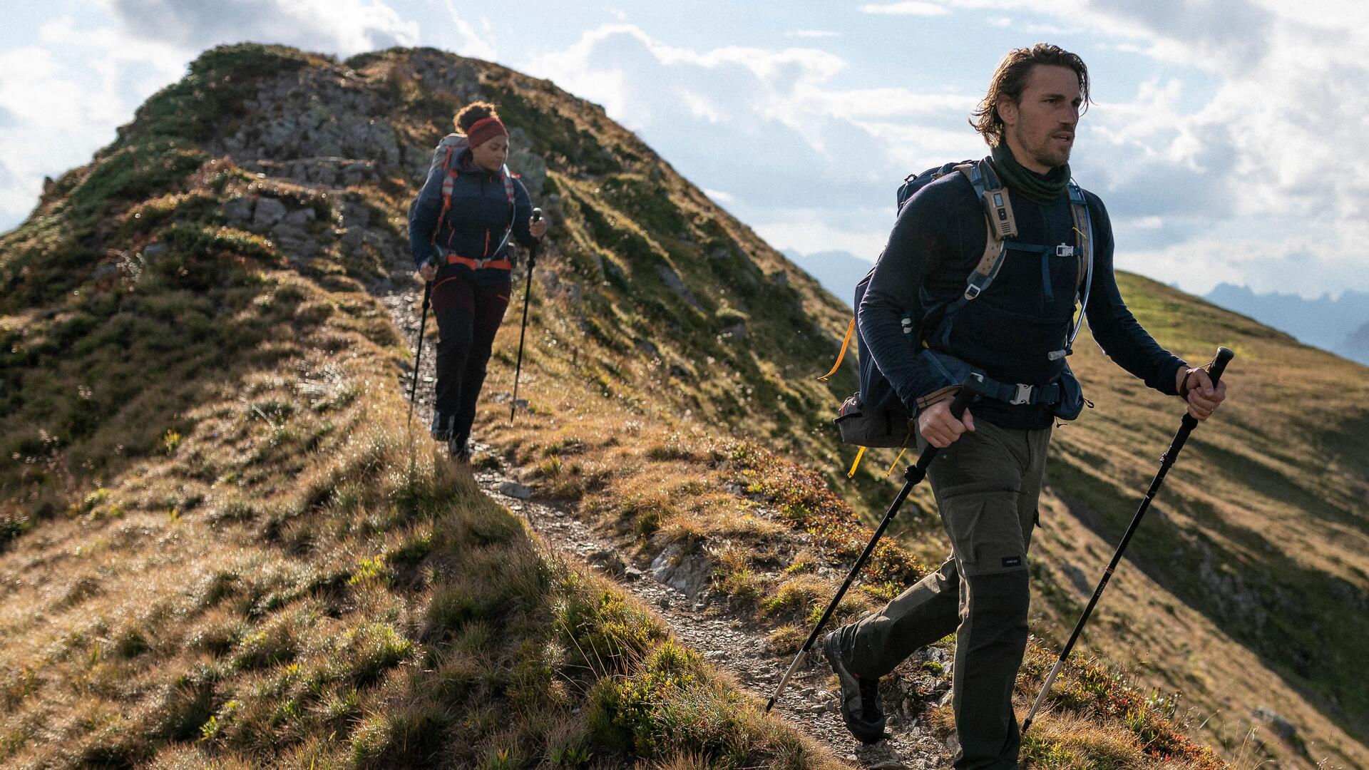 mężczyzna i kobieta idący po górach w butach trekkingowych  z kijkami trekkingowymi 