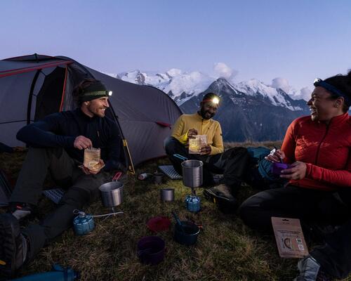 Man and woman sitting around backpacking stove and eating.