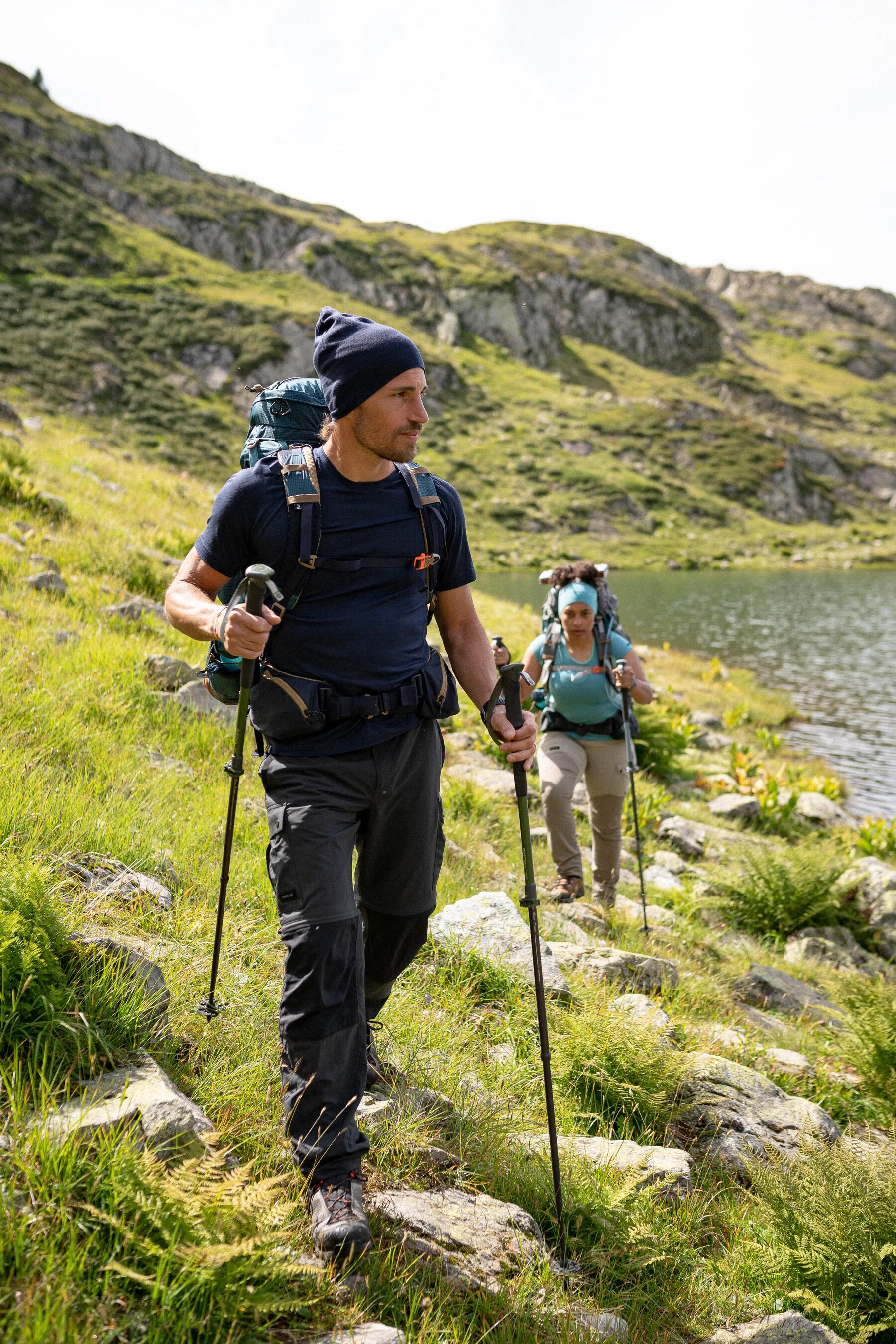 Mężczyzna i kobieta idący po górskim szlaku z kijkami trekkingowymi