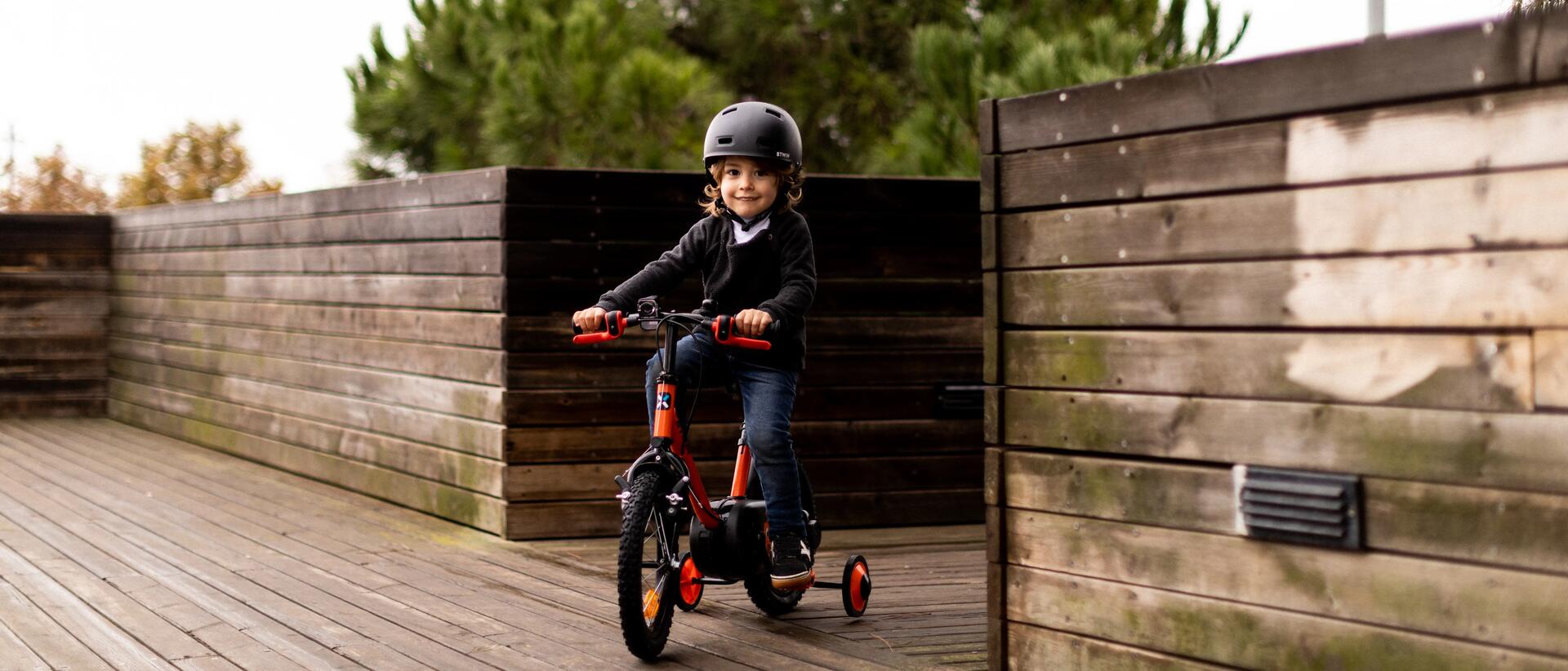dziecko w kasku jadące na rowerze z dodatkowymi kółkami
