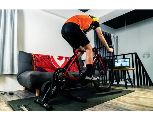 Mężczyzna trenujący na trenażerze rowerowym na platformie Zwift w pokoju