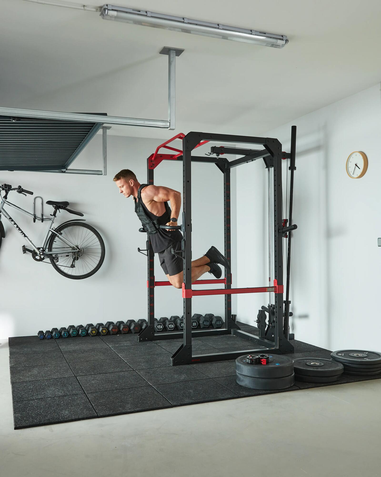 Ein Mann macht Dips an einem Kraftstation-Rack in einem hellen Home-Gym in einer Garage.