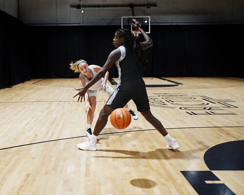 Two women playing basketball in indoor court