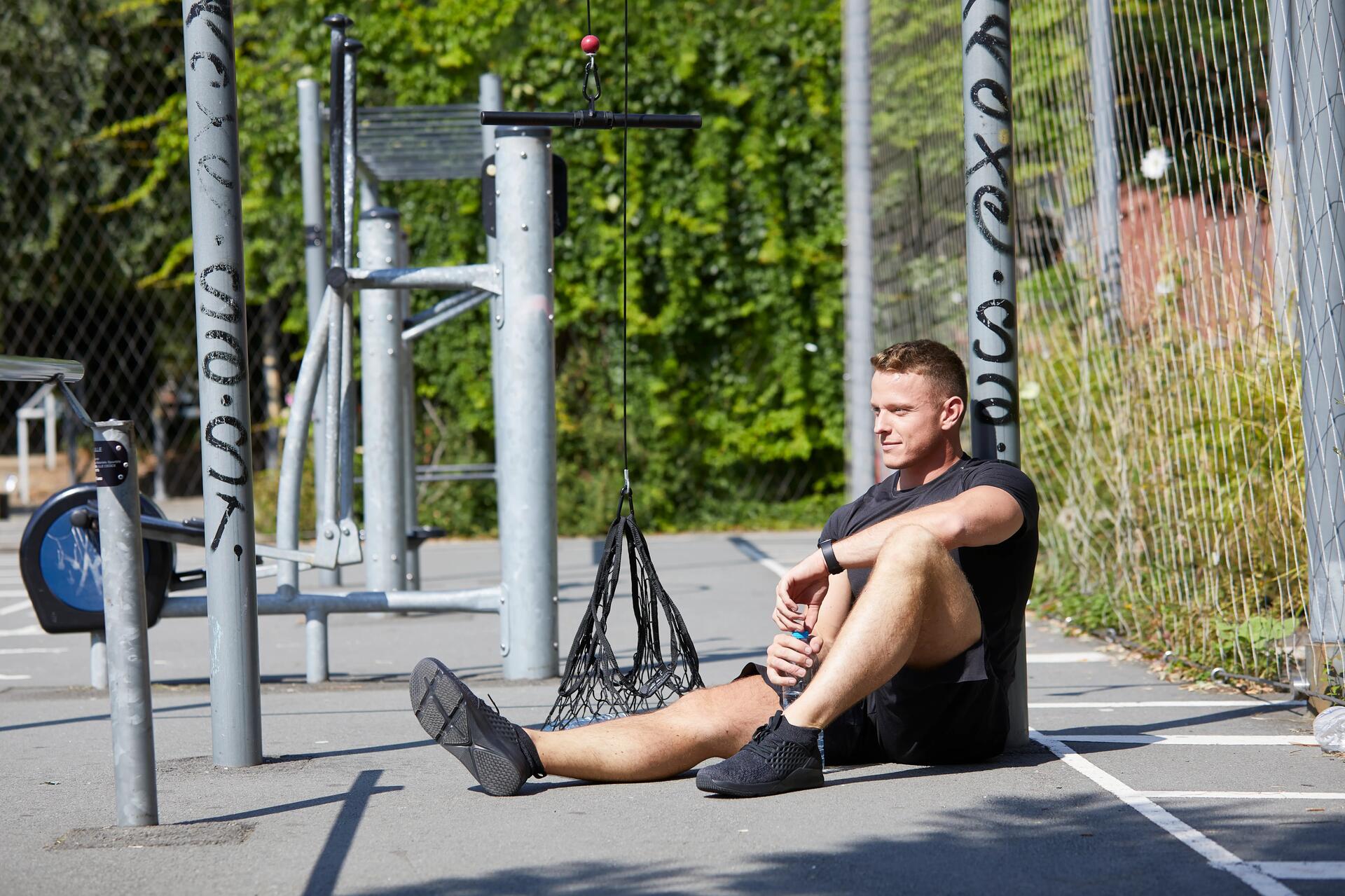 Mężczyzna w odzieży sportowej odpoczywający po treningu siedząc na ziemi z butelką w dłoni