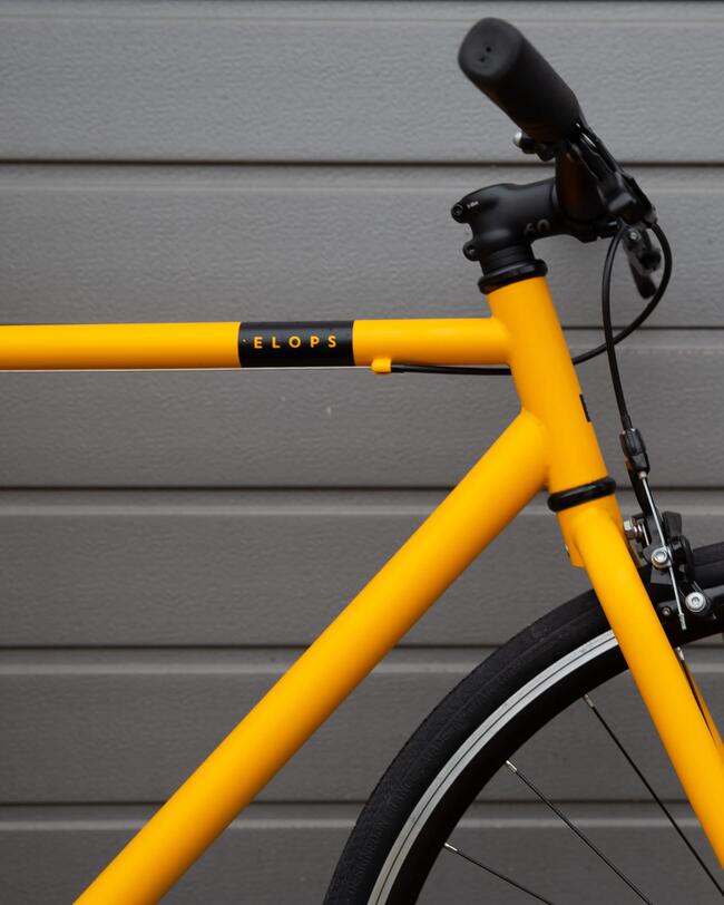 Gelbes Fahrrad mit schwarzem Lenker vor grauer Hauswand