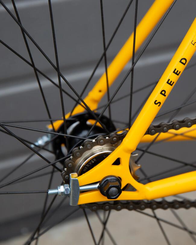 Detailaufnahme Ein-Gang-Schaltung am Hinterrad an gelben Fahrrad; vor grauer Hauswand