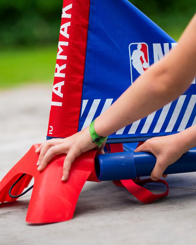Roter und blauer Kinder-Basketballkorb mit stabiler Basis, Hände justieren den Ständer, helle Farben, glatte Texturen.