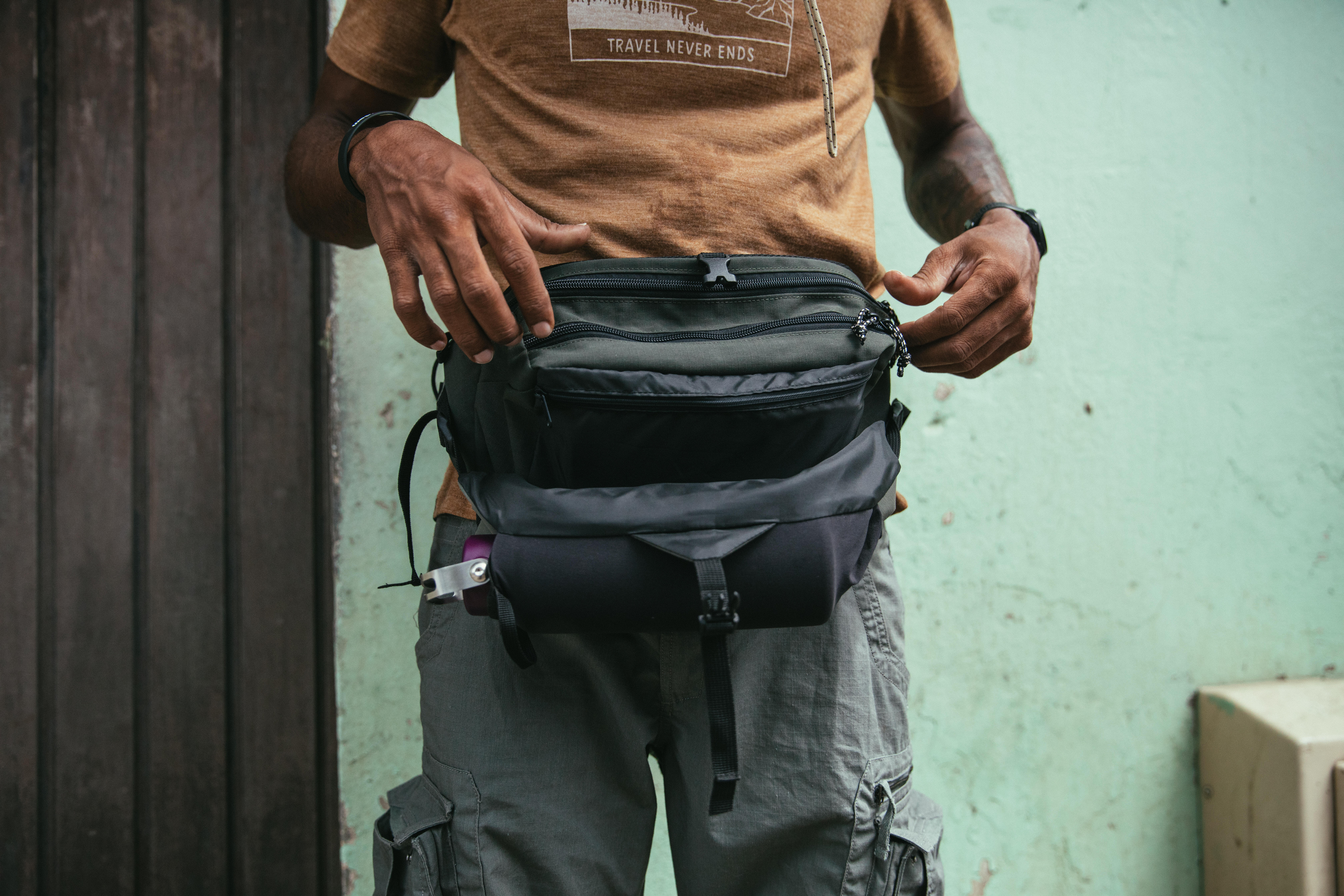 Hiker wearing a black waist bag with multiple compartments and adjustable straps.