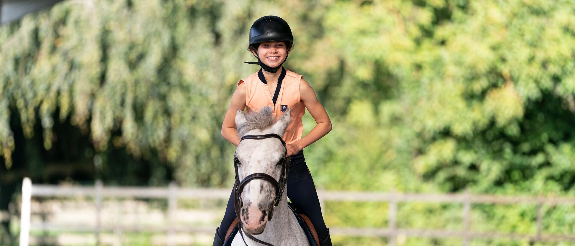 A little girl riding on a Horse wearing a Helmet