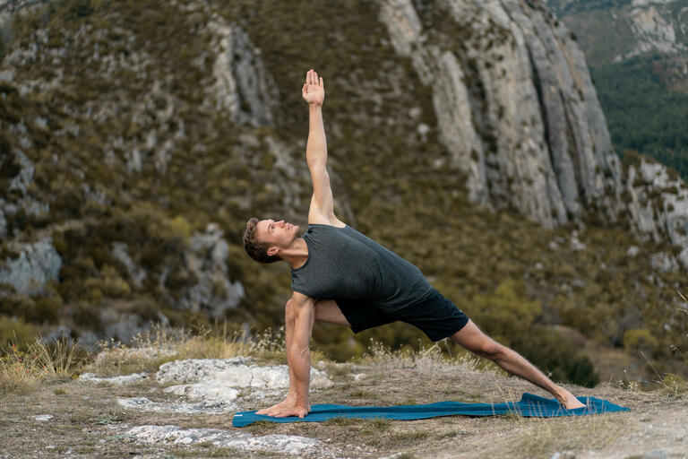 Man wearing a dark grey yoga top and shorts practising yoga outdoors