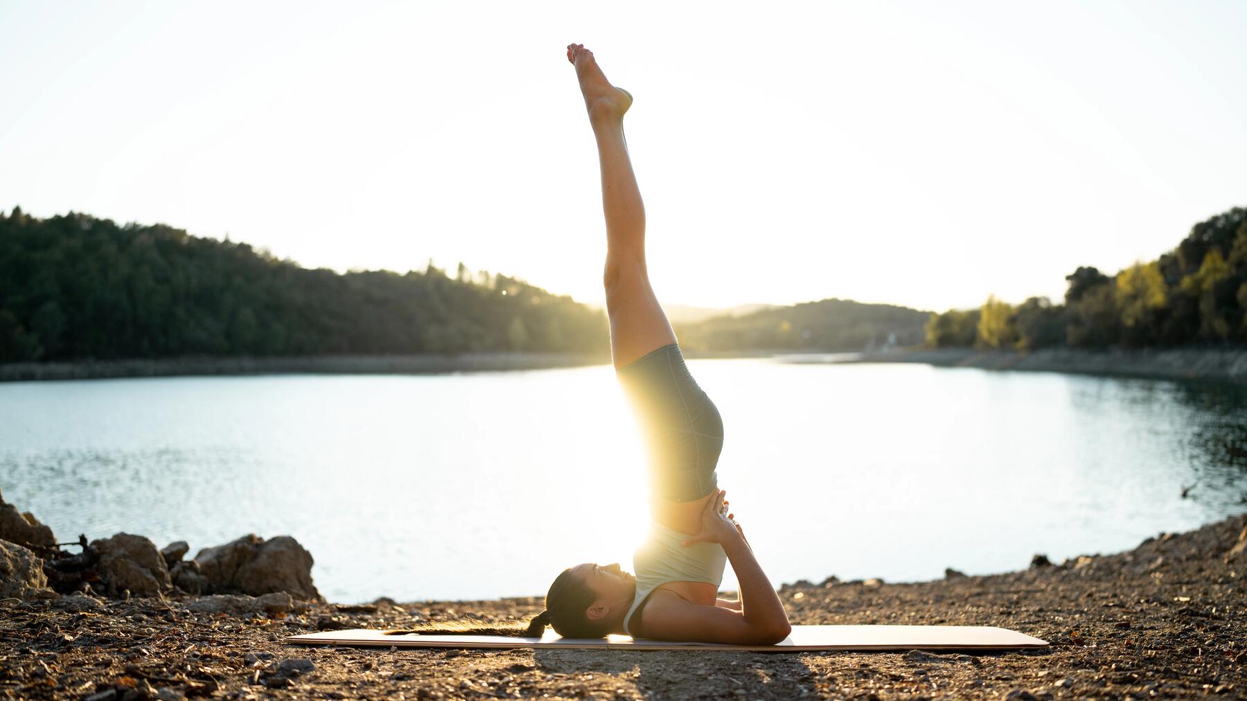 Frau in kurzer Yogabekleidung auf Yogamatte vor einem See beim morgendlichen Yoga