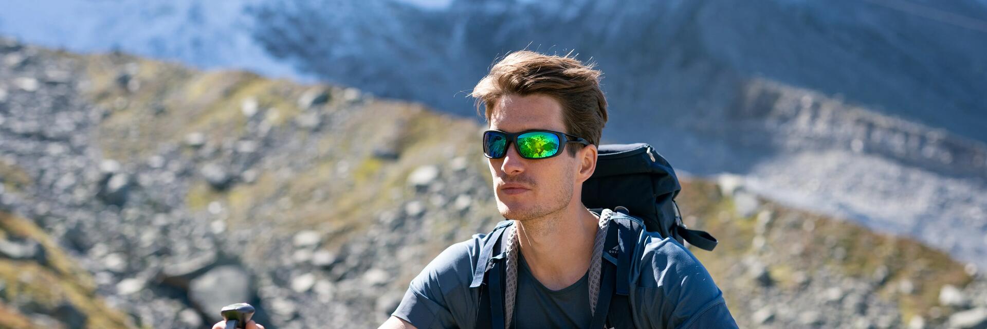 Mężczyzna wędrujący szlakiem górskim w okularach przeciwsłonecznych w góry z plecakiem turystycznym na plecach