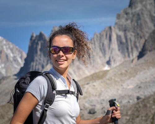 kobieta wędrująca po górach w okulach przeciwsłonecznych z kijami trekkingowymi w rękach