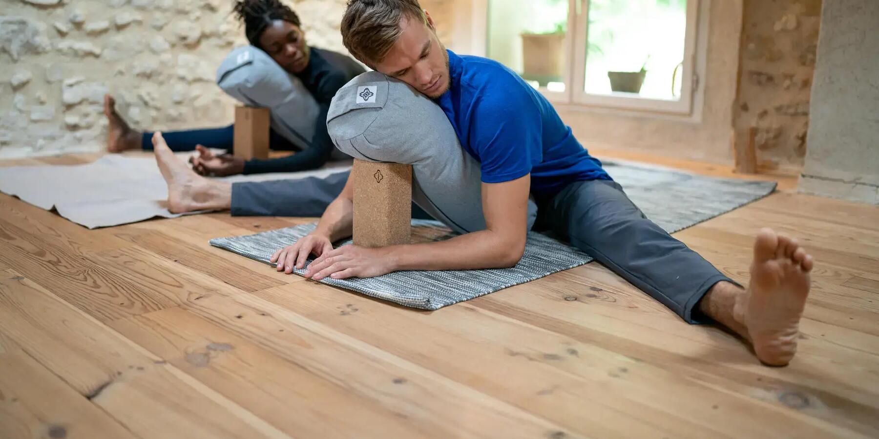 A couple stretching and meditating with on a Yoga black with a Yoga Bolster.