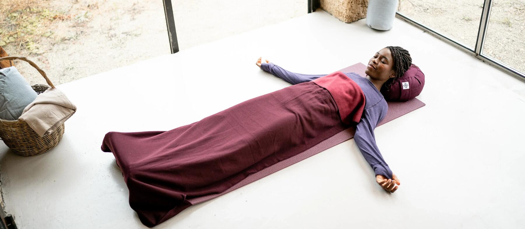 A woman meditating on a Yoga mat, with a Yoga cushion and a Yoga Blanket