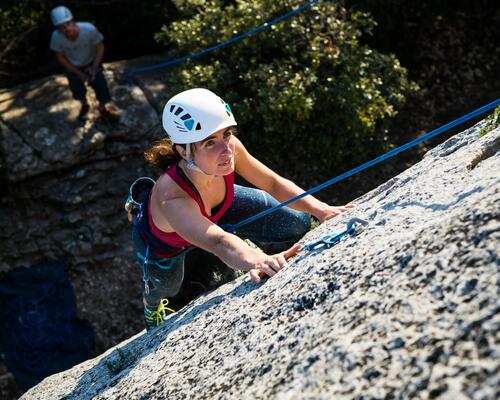 Kobieta w kasku wspinaczkowym wspinająca się po skale z użyciem liny wspinaczkowej