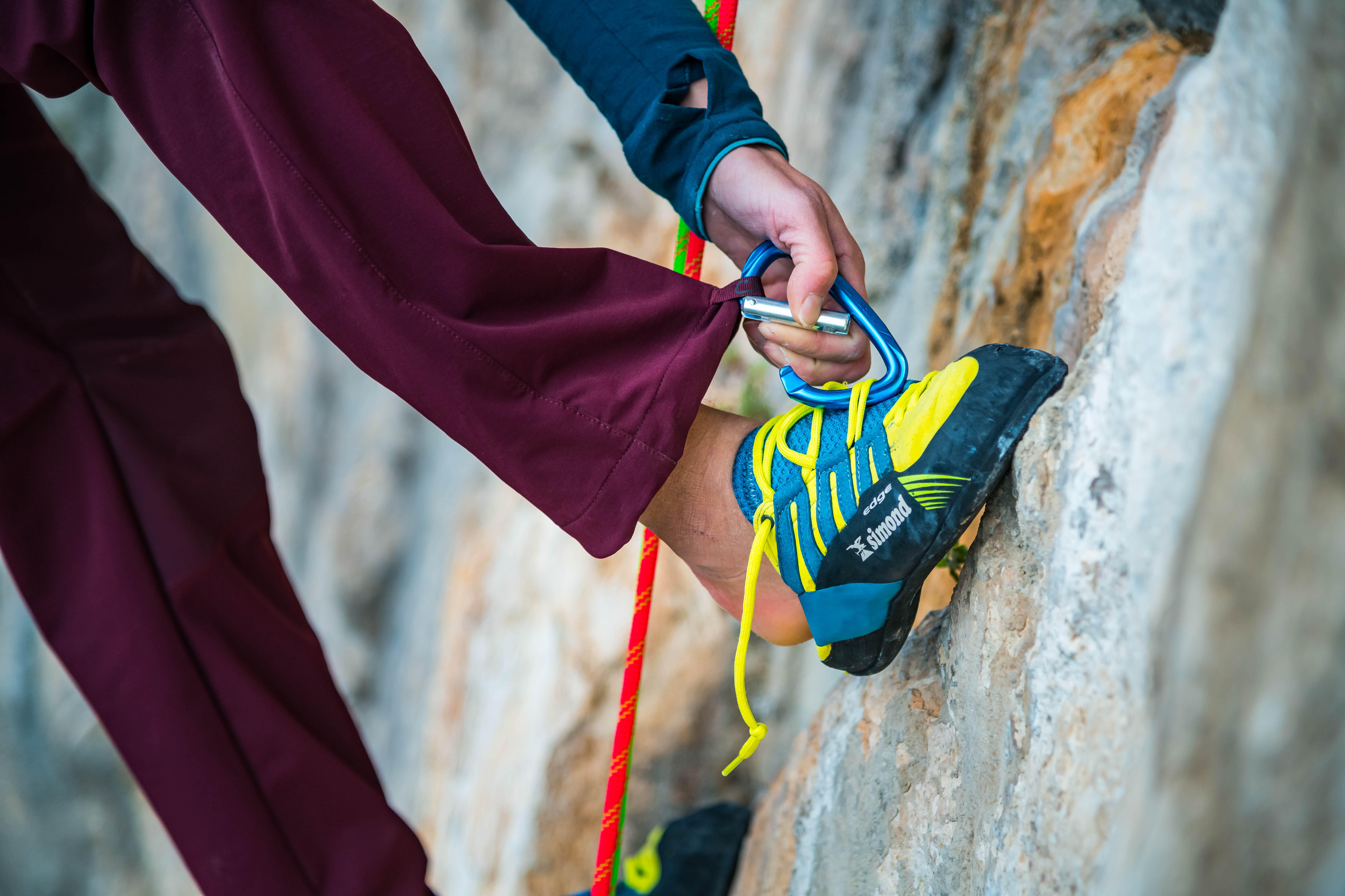 Rock climber clipping a carabiner while wearing climbing shoes on a rock face.