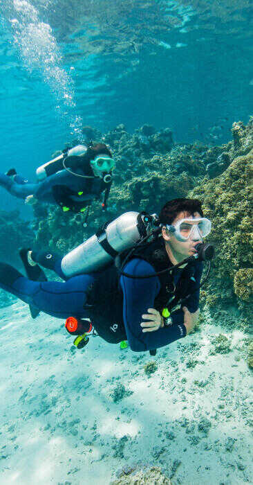 muž ktory sa potápa s prístrojom pri korálovom útese