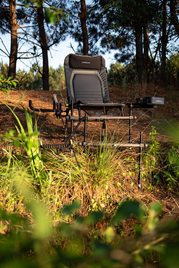 Profesionalni Caperlan ribiški stol s podloženim sedežem in naslonom za glavo, opremljen s stranskimi držali za palice in policami za dodatke, postavljen v naravi.