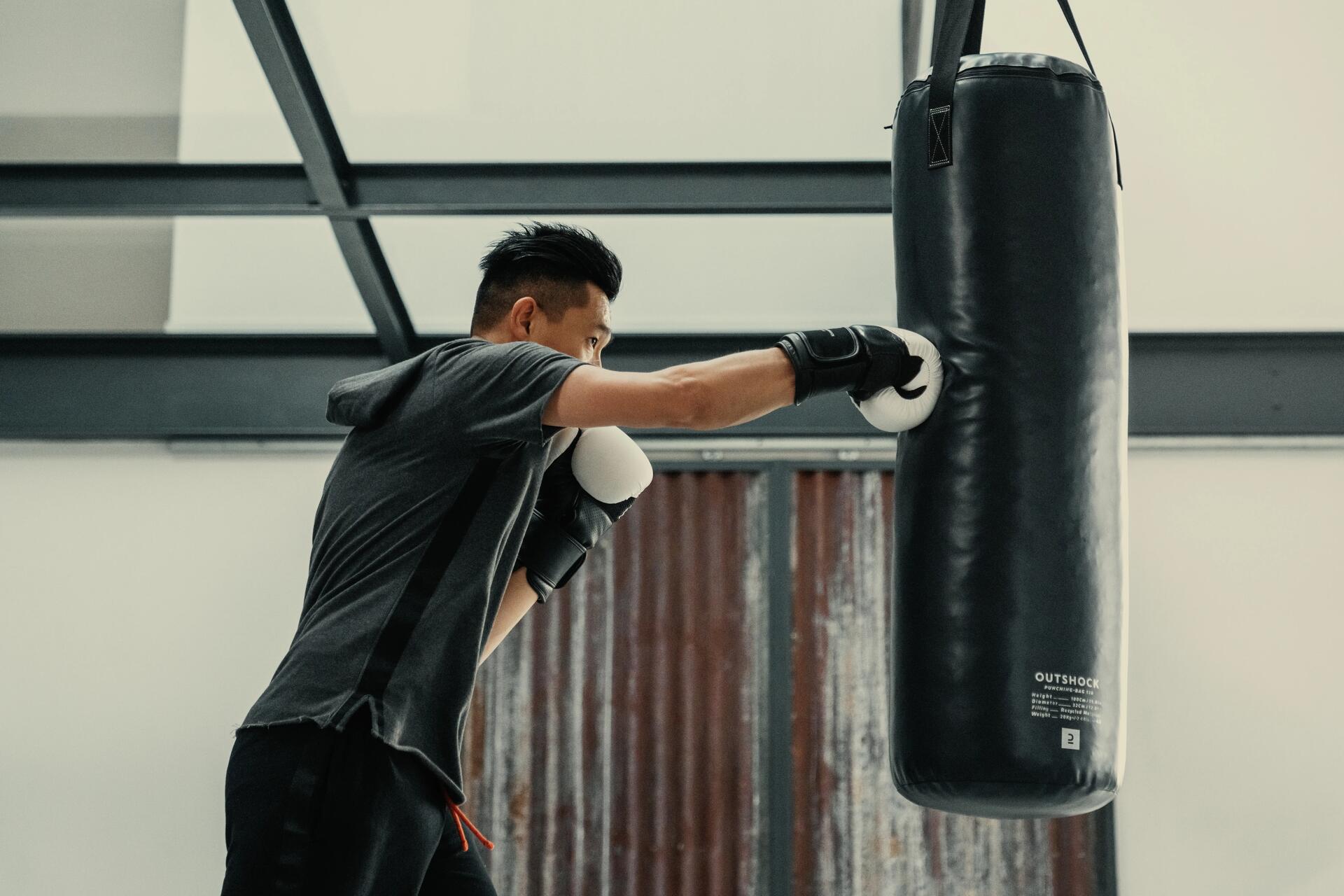 mężczyzna w odzieży sportowej trenujący na worku bokserskim w rękawicach bokserskich