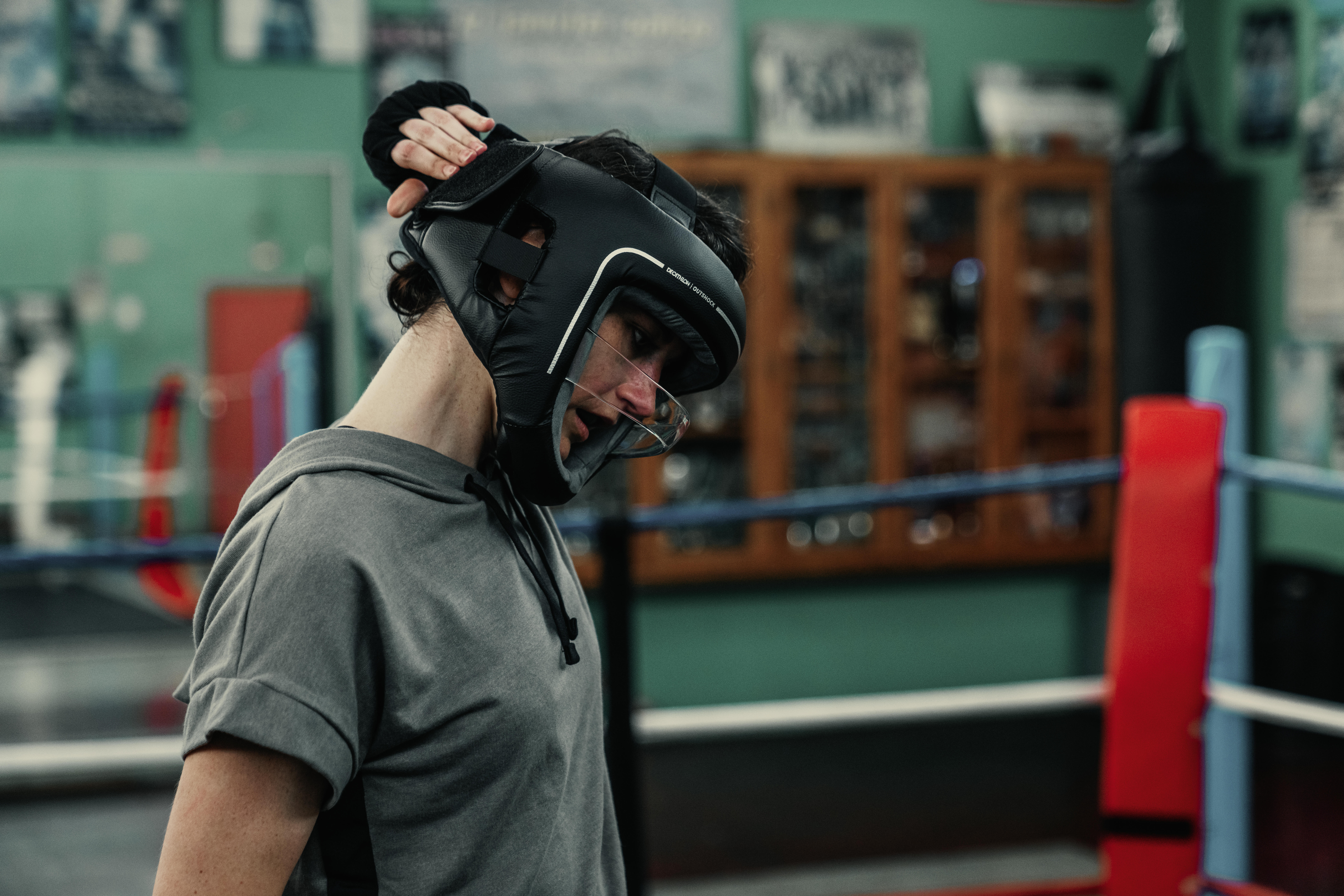 Boxer adjusting a black protective headguard with face shield in a boxing ring