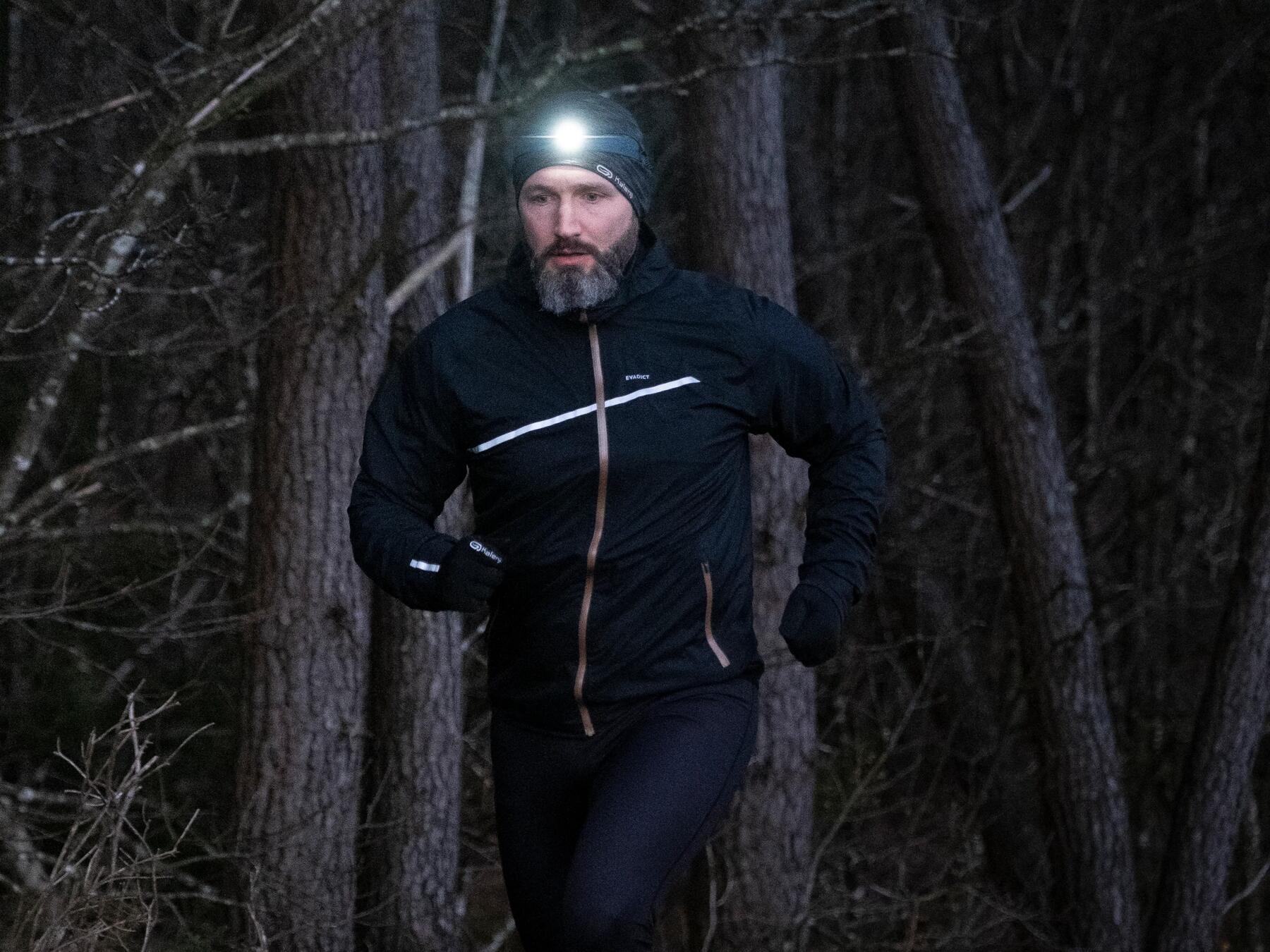 mężczyzna w odzieży biegowej biegnący wieczorem  lasem z latarką czołową na głowie