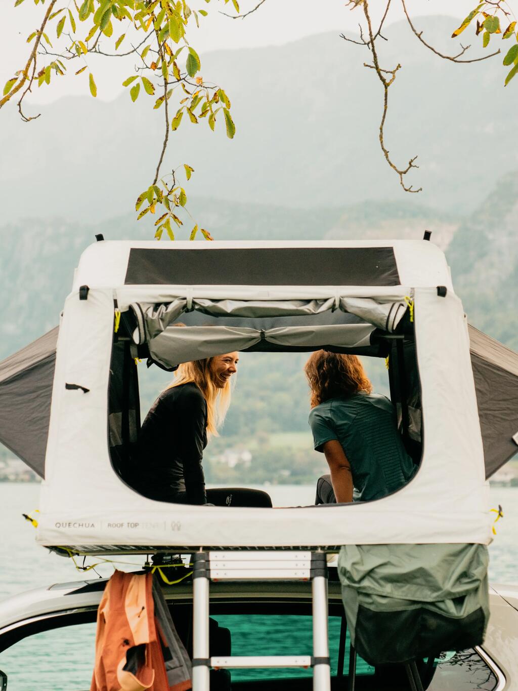 Ein Paar sitzt in einem Dachzelt und blickt auf einen See.