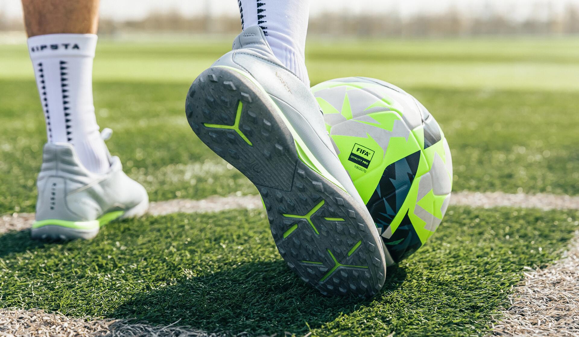 mężczyzna   w butach piłkarskich stojący na murawie z piłką nożną