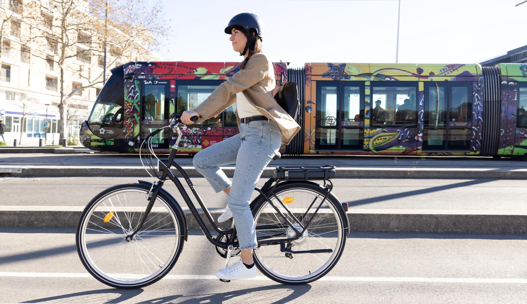 woman riding an Elops fully-equipped e-bike alongside a tram train in the background