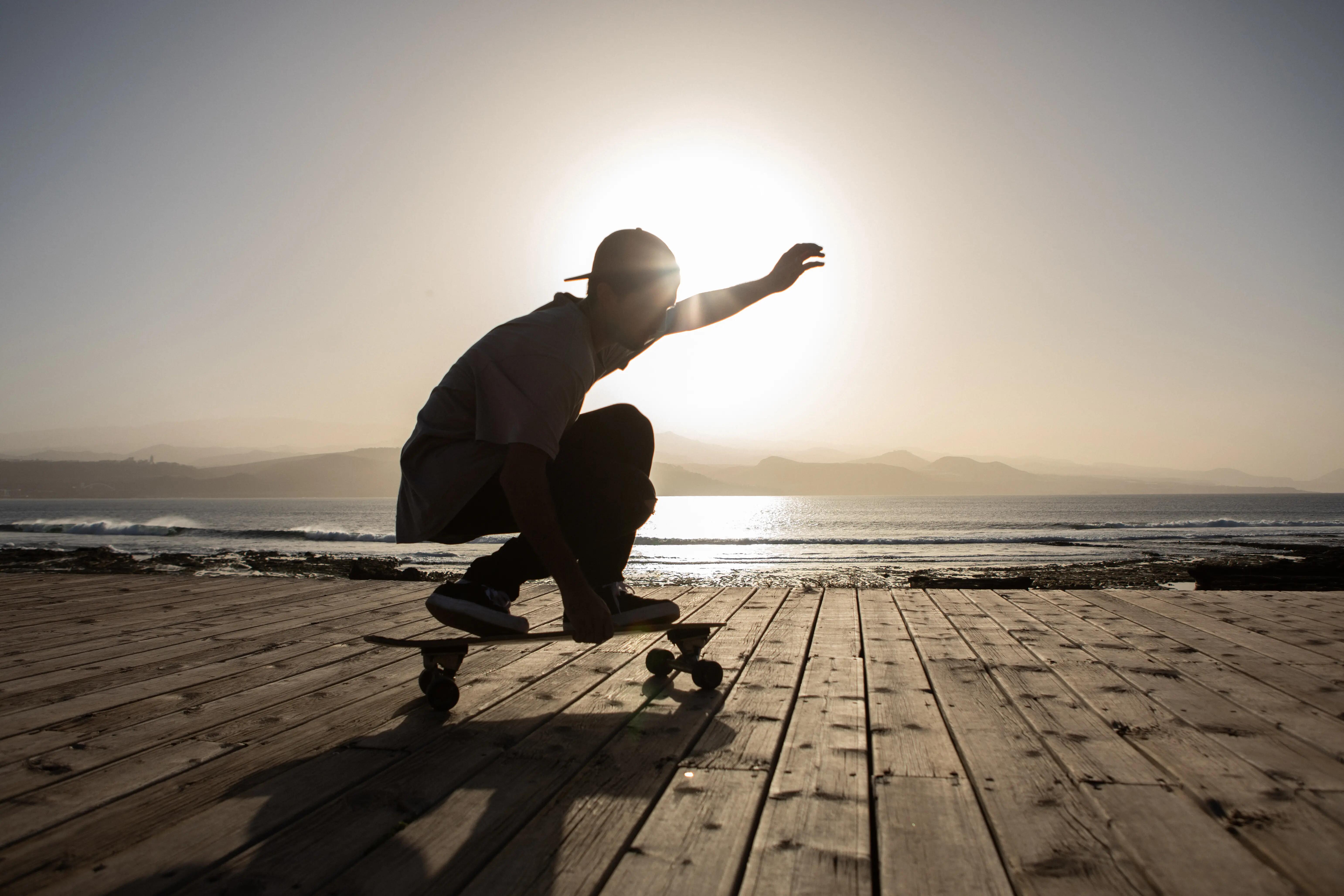 Silhouetted skater crouching on a longboard against a bright sunset