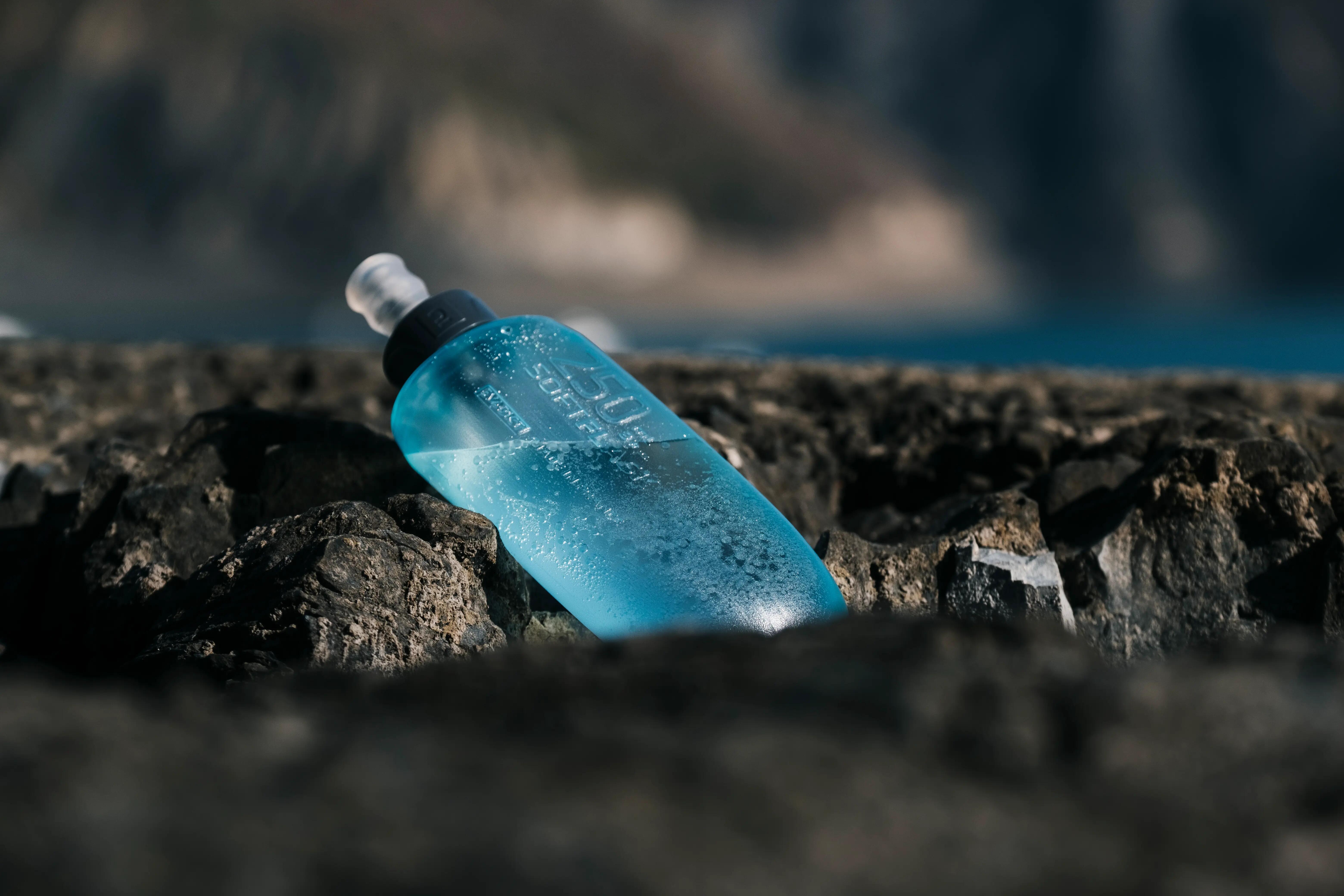 Blue soft water flask resting on rocks beside a mountain lake.