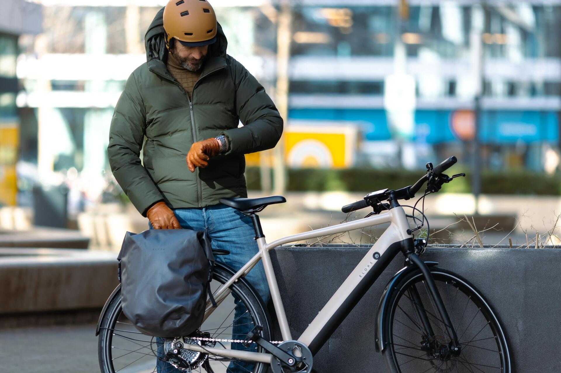 mężczyzna w kasku rowerowym patrzący na zegarek stojąc obok roweru elektrycznego
