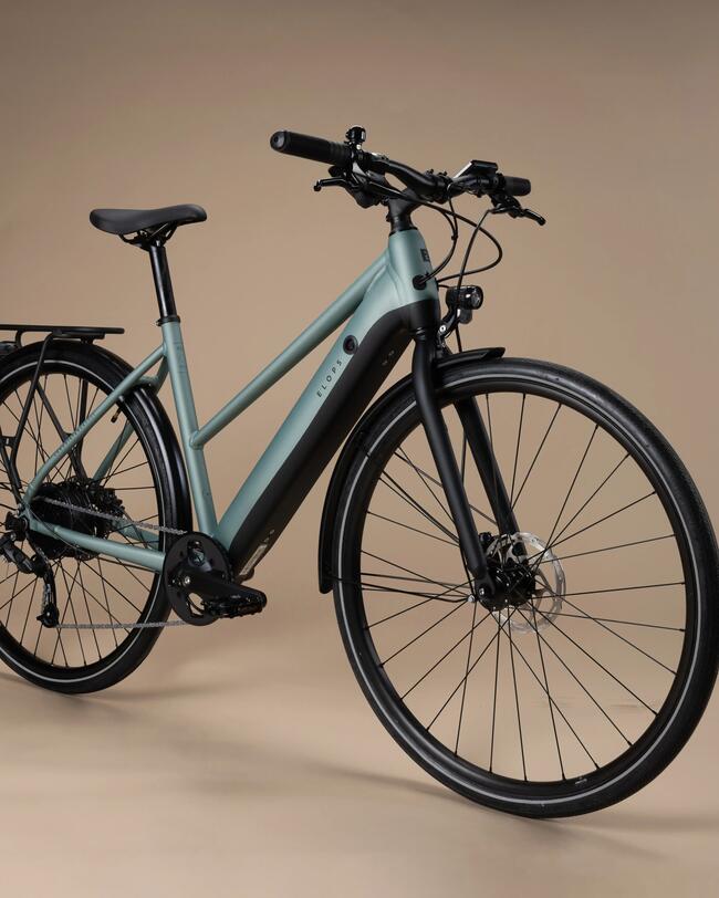 Grünes E-Bike mit schwarzen Details und Gepäckträger; beiger Hintergrund