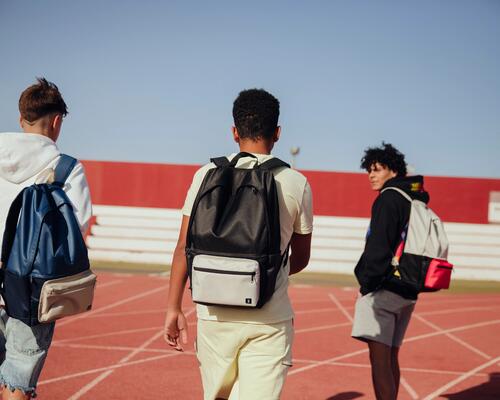 3 teenages walking across a running track with backpacks