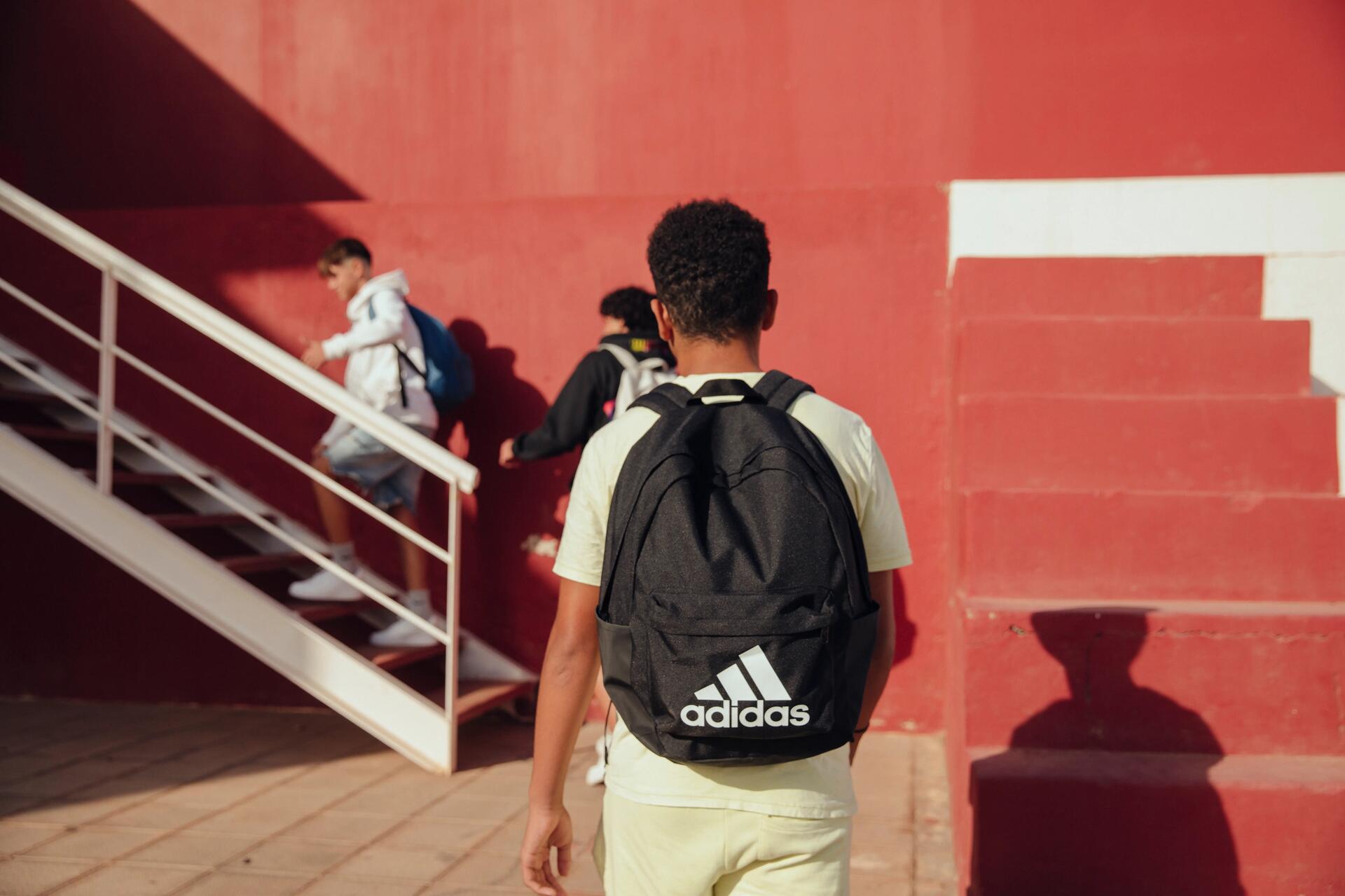 un elev care poartă un rucsac Adidas clasic în timp ce merge la școală